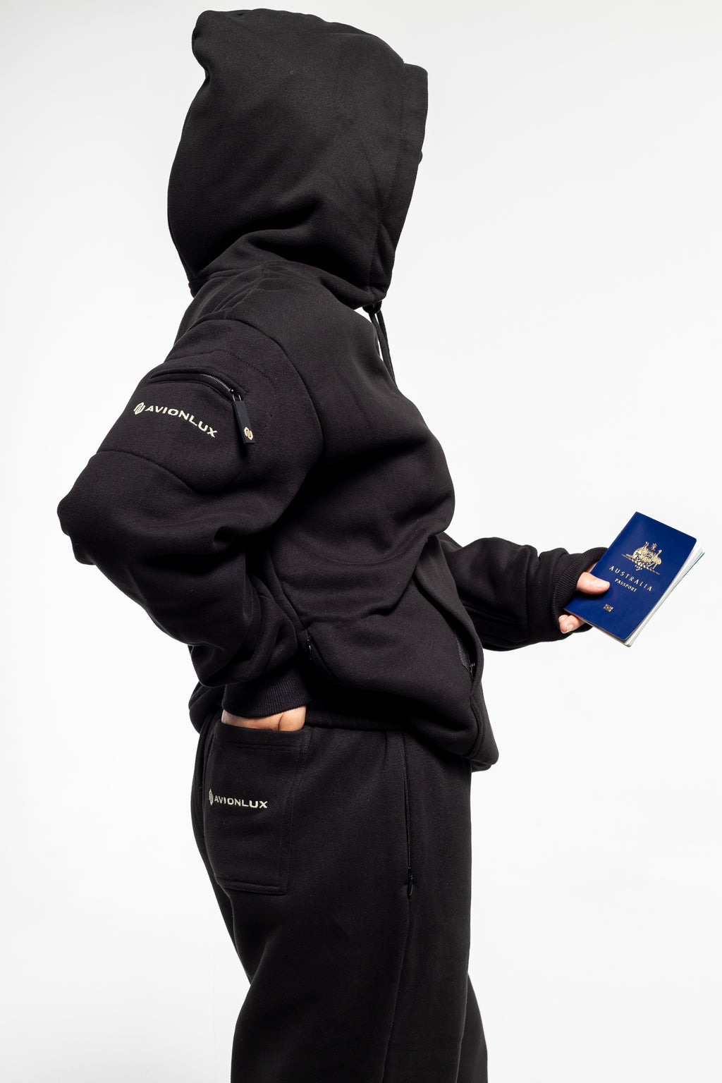 Person wearing a black hoodie with 'AVIONLUX' branding, holding a passport.