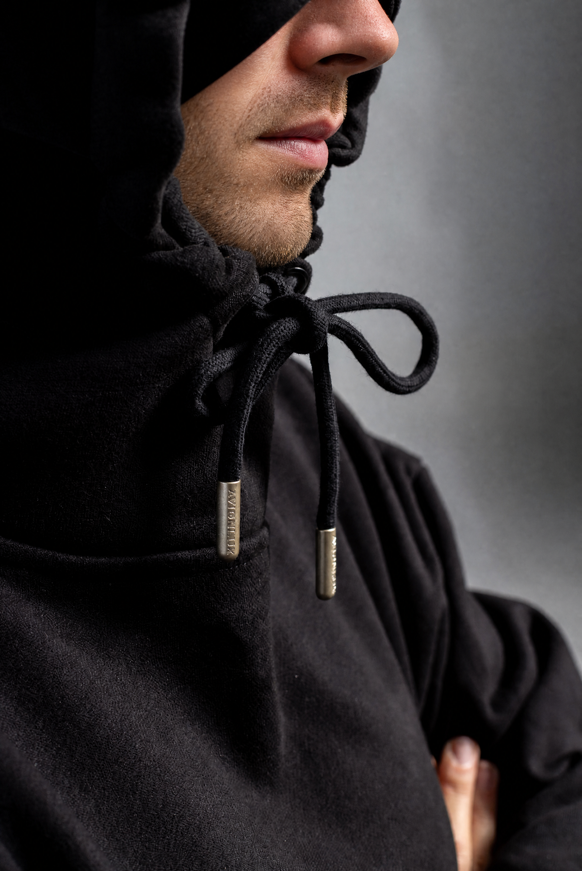 Close-up of a person wearing a black hooded sweatshirt with black drawstrings and small metallic silver tips, shown against a dark gray background.